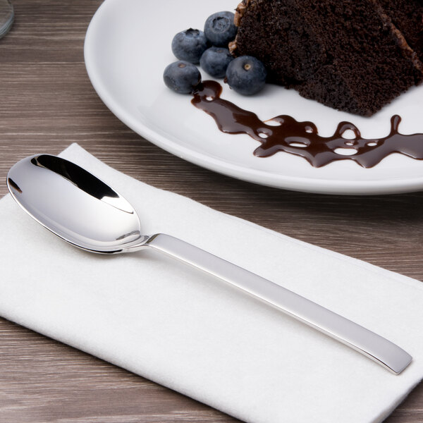 A plate with a spoon and a piece of chocolate cake with an Arcoroc stainless steel dessert spoon on a white napkin.