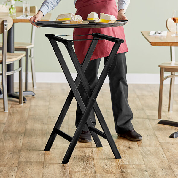A person holding a Lancaster Table & Seating black wood tray stand with food on it.