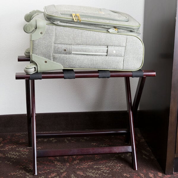 A mahogany wood Lancaster Table & Seating folding luggage rack holding a suitcase.