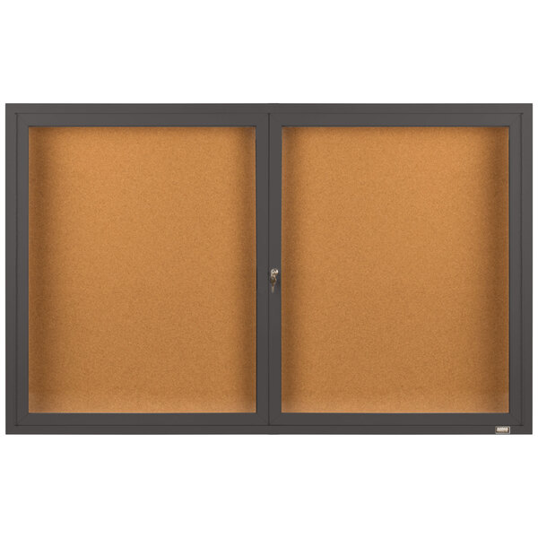 A brown rectangular Aarco bulletin board cabinet with two black enclosed glass doors.