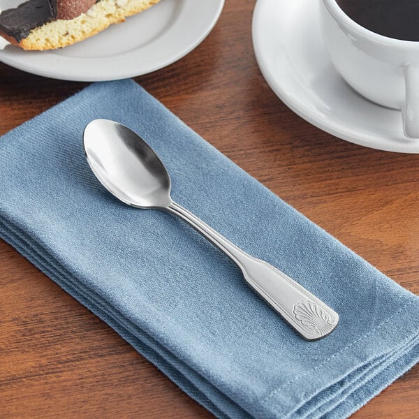 An Acopa stainless steel teaspoon on a napkin next to a white cup of coffee.