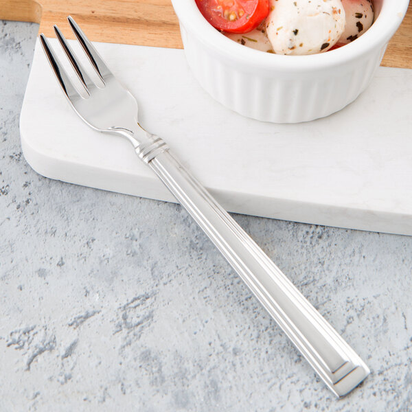 A Libbey stainless steel cocktail fork on a white plate with food.