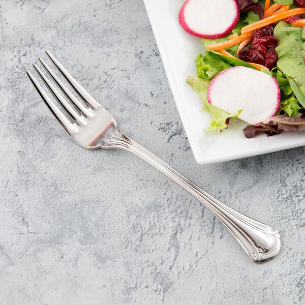 A World Tableware stainless steel salad fork with salad on it next to a plate.