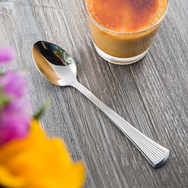 A Libbey stainless steel teaspoon next to a glass of liquid on a table.