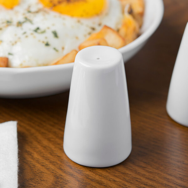 A Schonwald white porcelain pepper shaker next to a plate of food.