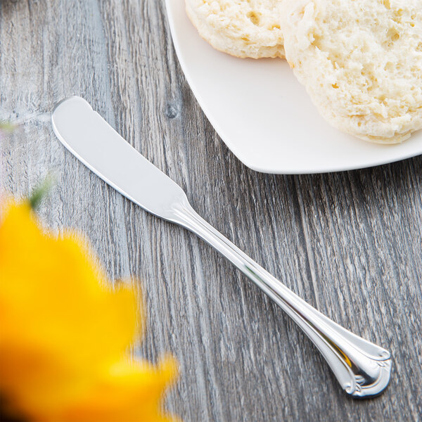 A World Tableware Resplendence stainless steel butter spreader on a plate next to a muffin.