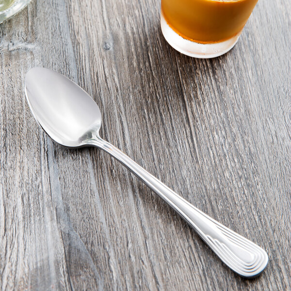 A Libbey stainless steel dessert spoon on a table next to a glass of juice.