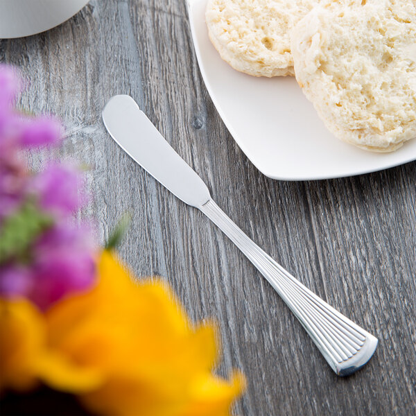A Libbey stainless steel butter spreader on a plate next to biscuits.