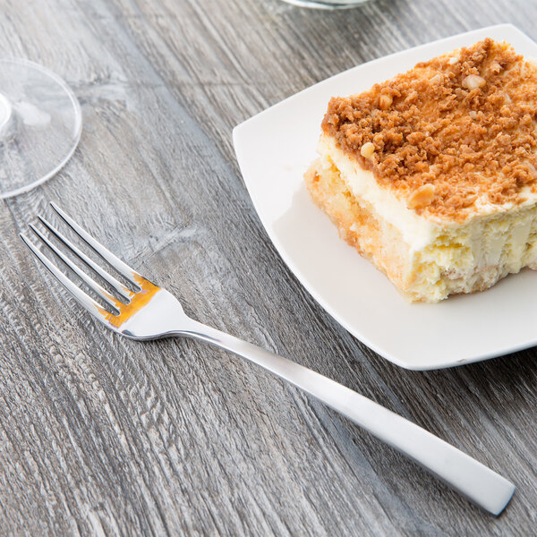 A Libbey stainless steel utility/dessert fork taking a bite of cake on a white plate.