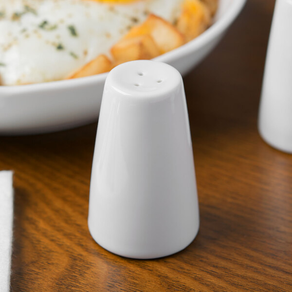 A Schonwald white porcelain salt shaker next to a plate of food.