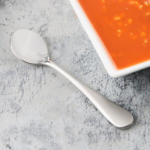 A Reserve by Libbey stainless steel bouillon spoon next to a bowl of soup.