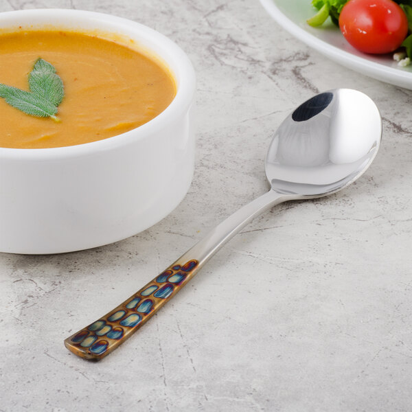 A bowl of soup with a Master's Gauge by World Tableware 18/10 stainless steel bouillon spoon.