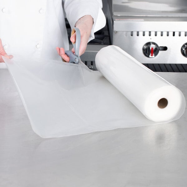 A person using scissors to cut a roll of VacPak-It full mesh plastic bags.