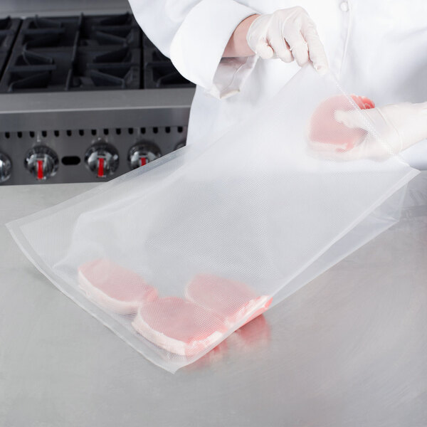 A person in white gloves using a VacPak-It gallon size full mesh vacuum packaging bag to hold meat.