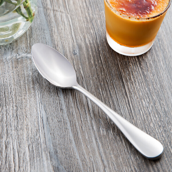 A Master's Gauge stainless steel teaspoon next to a glass of juice on a table.