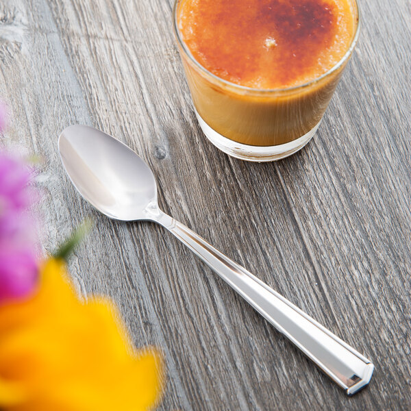 A Libbey stainless steel teaspoon on a table next to a glass of liquid.