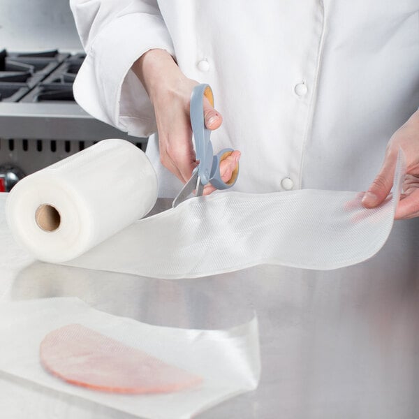 A person in a white coat cutting a piece of plastic with scissors.