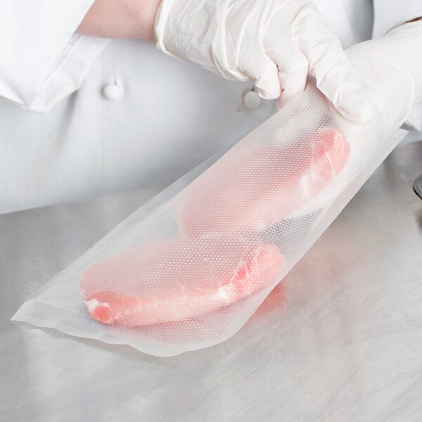 A gloved hand holds a VacPak-It vacuum packaging bag filled with meat.