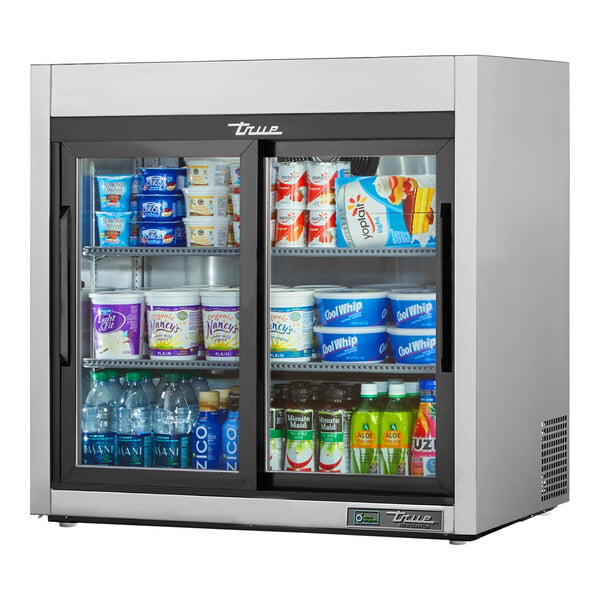A True stainless steel countertop display refrigerator with sliding glass doors filled with drinks and yogurt.