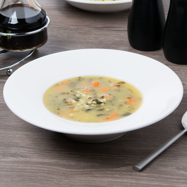 A white Villeroy & Boch porcelain bowl filled with soup and vegetables with a spoon on a table.