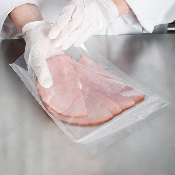 A person in gloves using a VacPak-It zipper vacuum packaging bag to put slices of ham in.