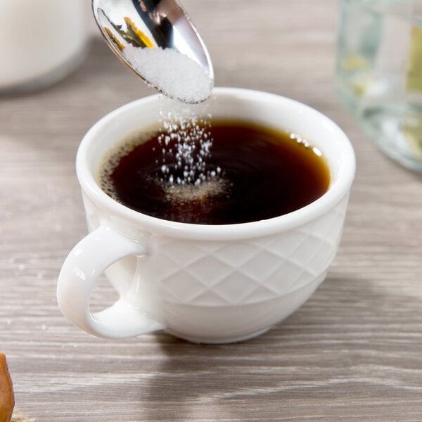 A spoon pouring sugar into a Villeroy & Boch white porcelain cup.