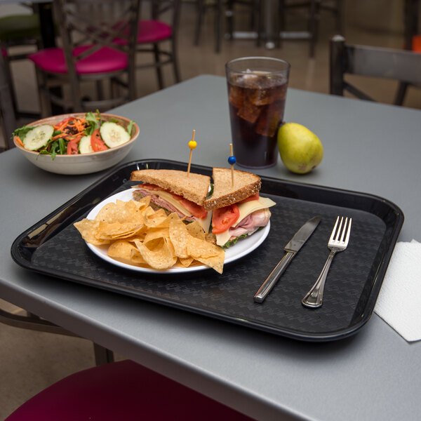 A Carlisle black plastic fast food tray with a sandwich, chips, and a drink on it.