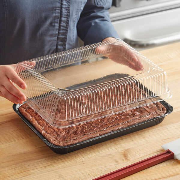 A person holding a clear plastic High Dome cover over a brown cake.