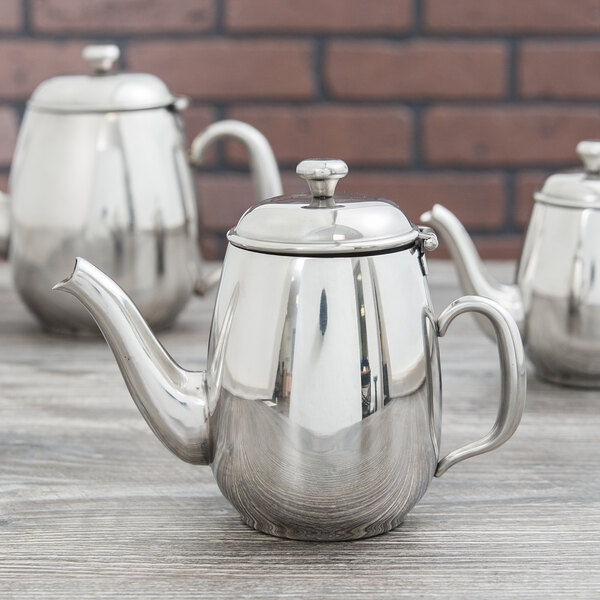 A group of Vollrath stainless steel teapots on a wood surface.