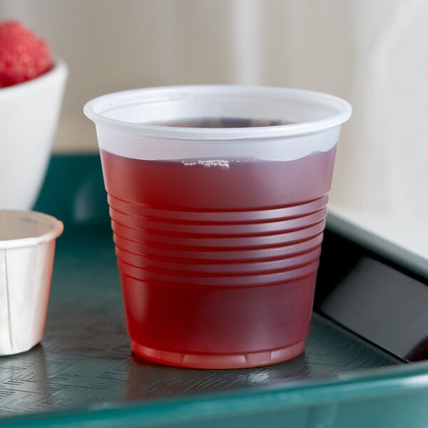 A Dart Conex translucent plastic cup with a red drink on a table.