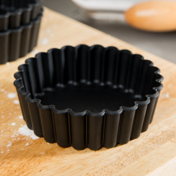 A black Matfer Bourgeat fluted tartlet mold on a wooden surface.