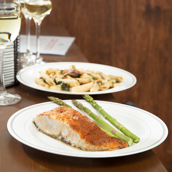 A white plastic plate with silver accent bands holding a piece of fish and meat with green asparagus on a table.