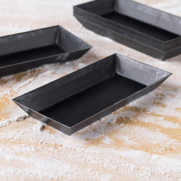Three black rectangular Matfer Bourgeat tartlet molds on a table.
