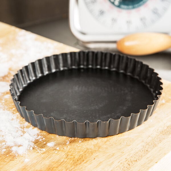 A black fluted tart pan with a scalloped edge.