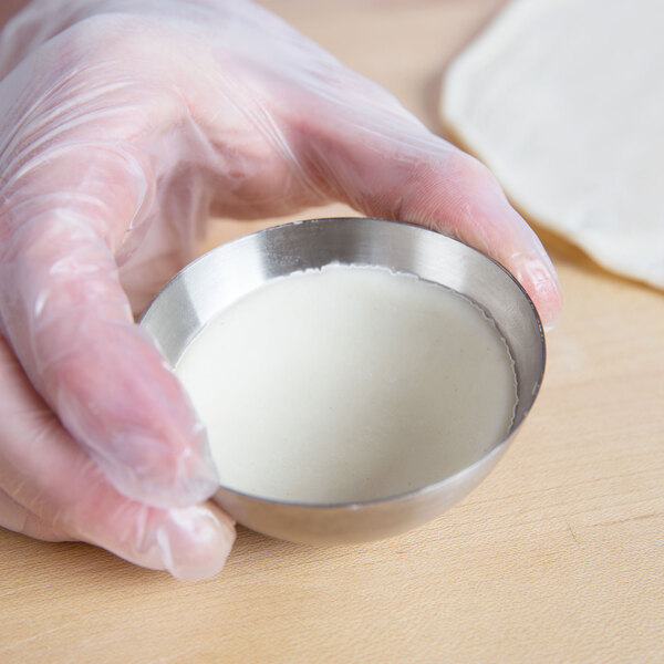 A person in gloves holding a bowl of dough.