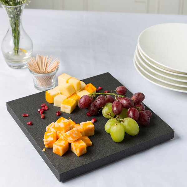 A black wooden display platter with cubes of cheese, grapes, and toothpicks.