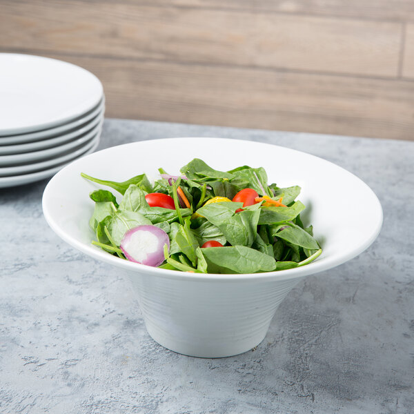 A white fluted melamine bowl filled with salad and vegetables.