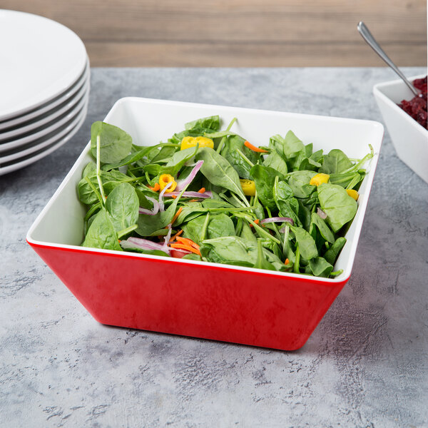 A red and white Vollrath melamine bowl filled with spinach salad on a table.