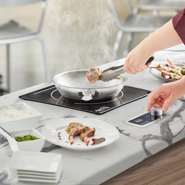 A woman using an Avantco countertop induction range to cook meat.