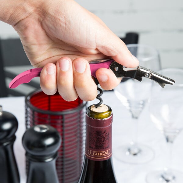 A hand using a Pulltap's Original customizable dark pink corkscrew to open a wine bottle.