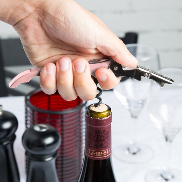 A hand holding a Pulltap's Original light pink Waiter's Corkscrew opening a bottle of wine.