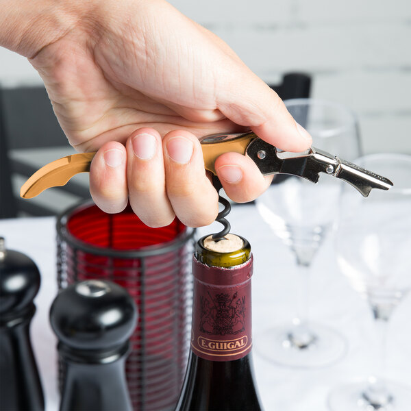 A hand with a hazelnut-handled Pulltap's Original corkscrew opening a bottle of wine.