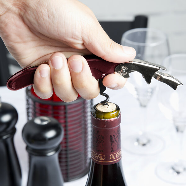 A hand using a Franmara two-lever corkscrew to open a bottle of wine.