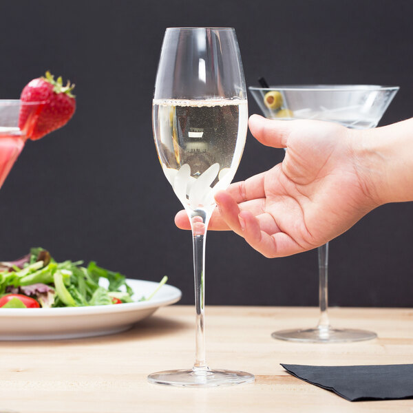 A hand holding a Reserve by Libbey Bloom Champagne Flute full of liquid next to a plate of food.