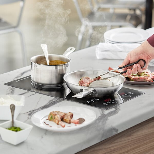 A person using an Avantco countertop induction range to cook food in a pan.