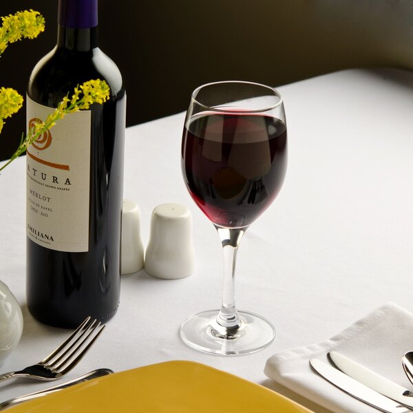 A Stolzle white wine glass and a bottle of wine on a table.