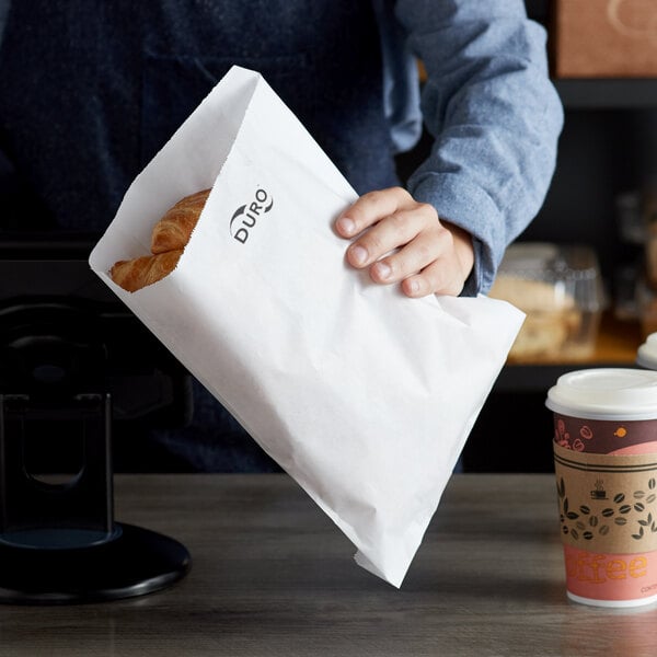 A person holding a croissant in a Duro paper bag.