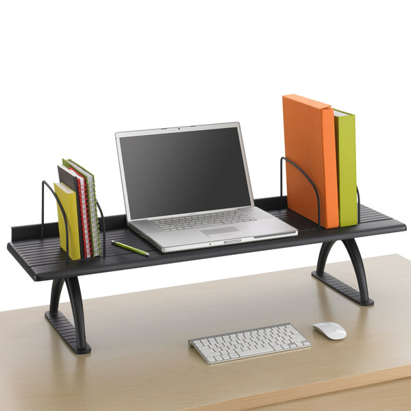 A Safco black monitor riser on a table with a laptop on it.