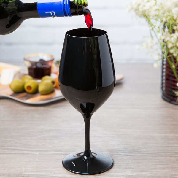 A Spiegelau Authentis black wine tasting glass filled with wine being poured from a bottle.