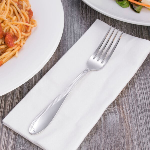 A Oneida Scroll stainless steel dinner fork on a napkin next to a plate of food.